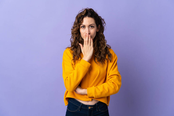 Young caucasian woman isolated on purple background covering mouth with hand - Foto, Imagem