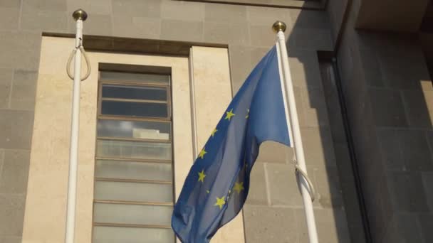 Σημαία της Ευρωπαϊκής Ένωσης κυματίζει στον άνεμο έξω από ένα κτίριο, έννοια της ένωσης και της ελπίδας - Πλάνα, βίντεο