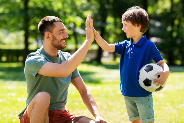 father giving five to son with soccer ball at park - Фото, изображение