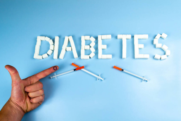 Na palcu wskazującym - ikonie cukrzycy - niebieskie kółko i strzykawki z insuliną, na tle napisu cukrzyca. Światowy Dzień Cukrzycy - Zdjęcie, obraz