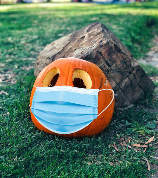 A carved pumpkin halloween wearing a face mask at a field outdoors. - Photo, Image