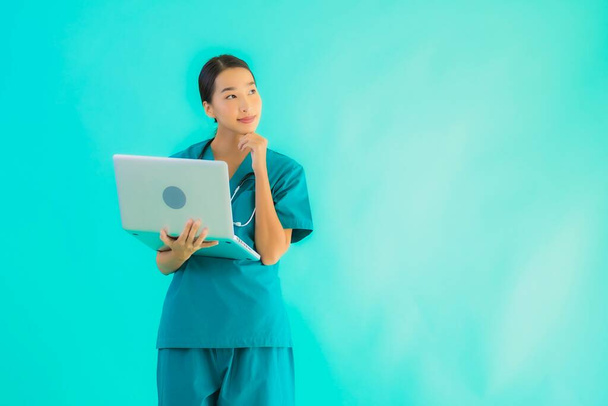 Retrato hermosa joven asiática médico mujer con portátil o computadora en azul aislado fondo
 - Foto, Imagen