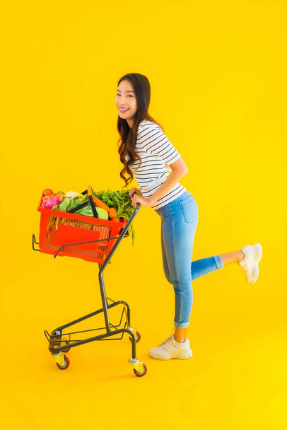 Retrato bonito jovem asiático mulher compras supermercado e carrinho no amarelo isolado fundo
 - Foto, Imagem