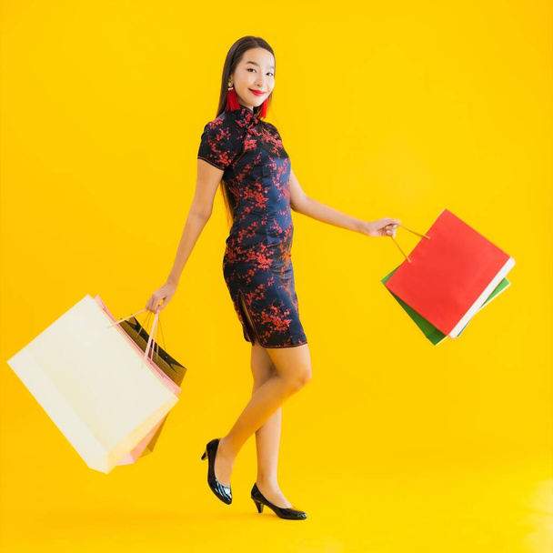 Портрет красивая молодая азиатская женщина носить китайское платье с сумкой, смартфон, кредитная карта для китайского нового года на желтом изолированном фоне
 - Фото, изображение