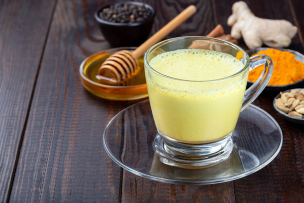 Moon milk with turmeric in a glass cup, ingredients on background, horizontal, copy space - Foto, imagen