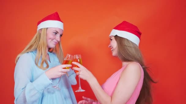 két fiatal nő visel karácsonyi sapkát piros háttér pirítóssal együtt és barátok - téli ünnepek koncepciók - Felvétel, videó