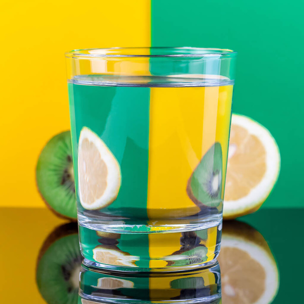 Illusion optique avec kiwi et citron déformée à travers le verre d'eau, fond jaune et vert, format carré - Photo, image