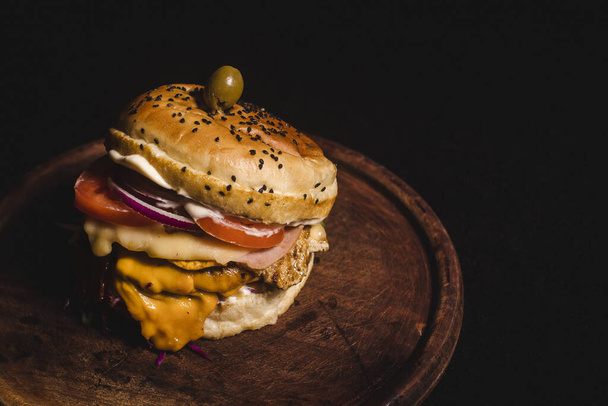 A closeup shot of an appetizing cheeseburger with meat and vegetables served on a wooden board - Zdjęcie, obraz
