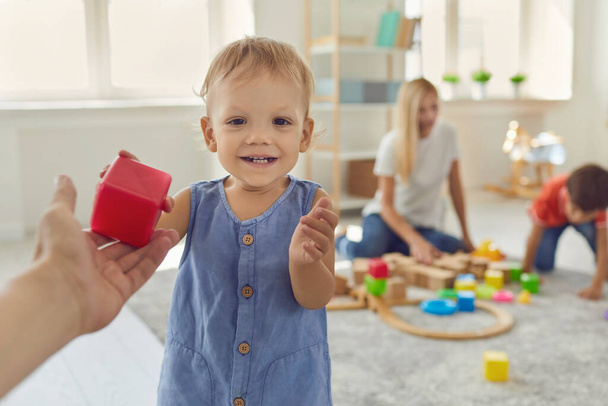Happy little boy gives a red plastic cube in the hands of his dad in a bright room. - Foto, imagen
