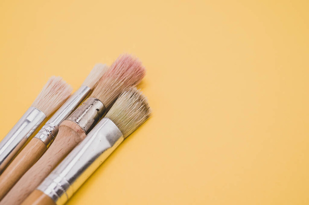 A closeup high angle shot of paintbrushes on a yellow surface - Fotó, kép