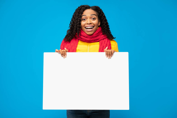 陽気なアフリカ人女性が青い背景に立って空のポスターを保持 - 写真・画像