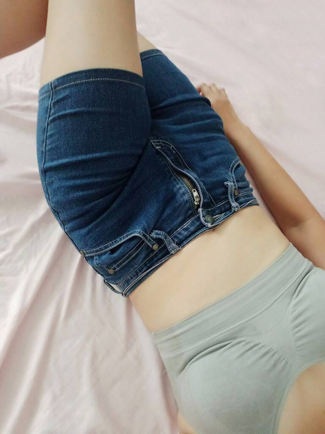 Uma jovem deitada na cama, usar calções jeans e sutiã esporte cinza. - Foto, Imagem