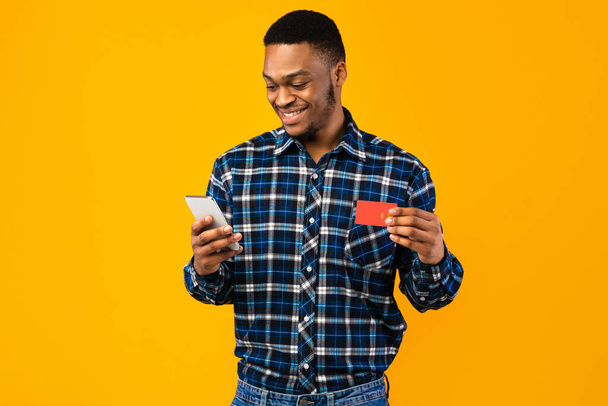 Щасливий чорний чоловік використовує смартфон тримає кредитну картку в студії
 - Фото, зображення
