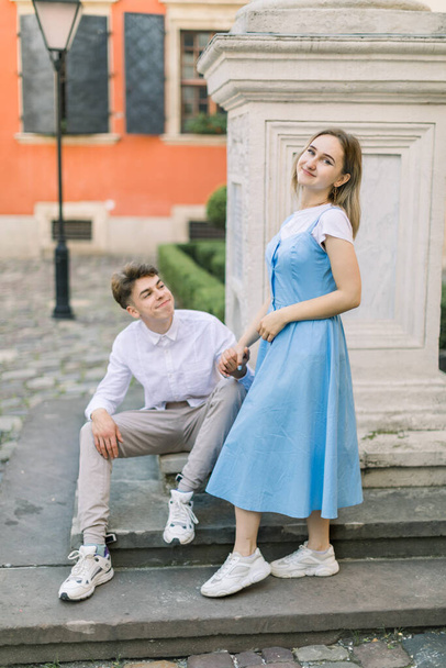 Love, relationships and people concept. Romantic date outdoors in the city of happy charming couple in love, standing on the stairs of monument in beautiful cozy yard with orange building - Foto, afbeelding