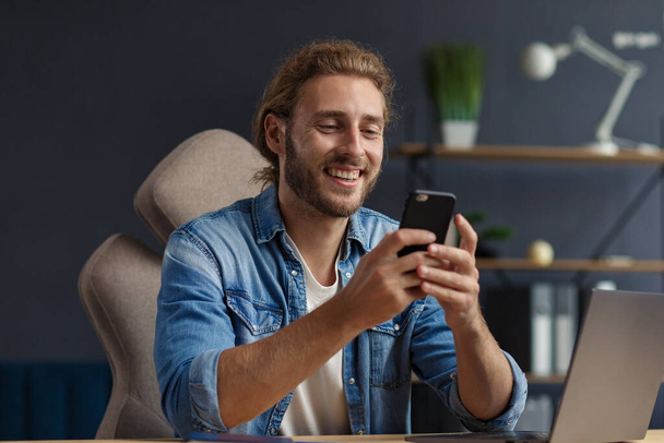 Young man using smartphone and smiling. Happy businessman using mobile phone apps, texting message, browsing internet, looking at smartphone. Concept of young people working with mobile devices - Foto, imagen