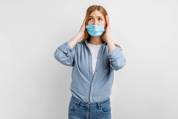 young woman in a medical mask on her face, holding her head in her hands, headache, on a white background - Foto, afbeelding
