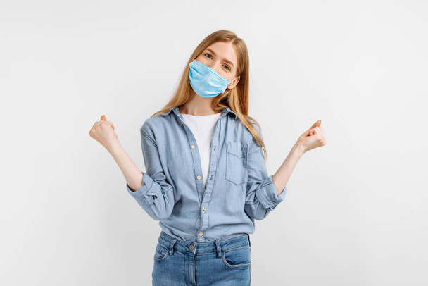 happy excited young woman in a medical mask on her face, shows a winning gesture on a white background - Photo, Image