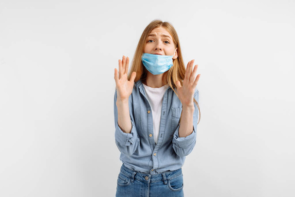 young woman in a medical mask on her face, holding her hand to her mouth and saying something confidential shares secret information, gossips rumors, on a white background - Photo, Image