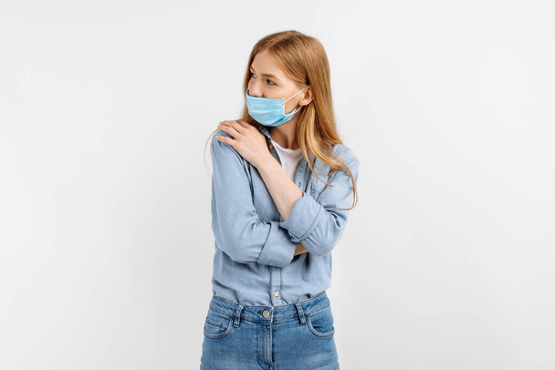Beautiful narcissistic young woman in a medical protective mask on her face, hugging herself on a white background - Photo, Image