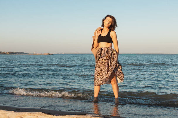 Retrato atmosférico de una mujer joven en falda elegante y abrigo caminando en la playa, en el mar de fondo. El concepto de libertad y emancipación femenina - Foto, Imagen