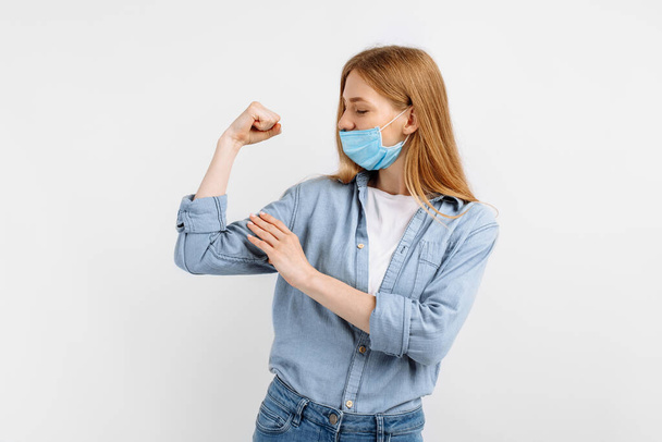 strong athletic young woman in a medical protective mask on her face, showing biceps on her arm, on an isolated white background - Foto, Bild
