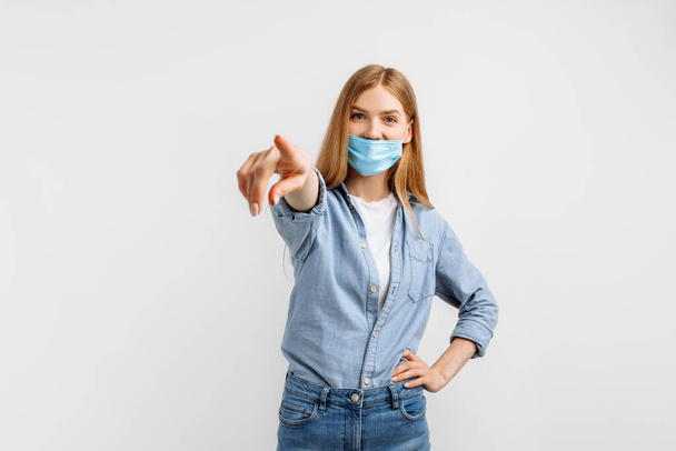 young woman in a medical protective mask on her face, pointing her finger into the distance, notices something amazing, on a white background - Foto, Bild