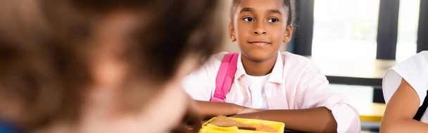 vízszintes termés afro-amerikai iskolás lány ül az iskolai étkezőben közelében uzsonnás doboz - Fotó, kép