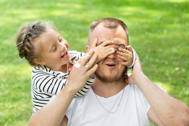 Family time. Father and daughter together. The girl covered her father's eyes with her hands. Surprise and surprise - Valokuva, kuva