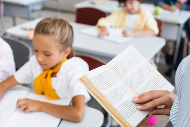 обрізаний вид вчителя читання книги біля учнів у класі
 - Фото, зображення