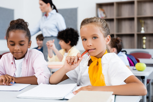 Вибірковий фокус школярки дивиться на камеру біля афроамериканського друга за столом у школі
  - Фото, зображення
