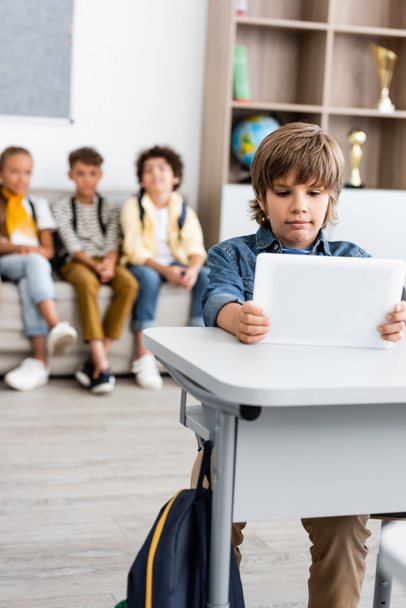 Selective focus of schoolboy holding digital tablet at desk in classroom  - Foto, afbeelding