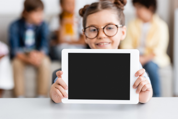 Selective focus of schoolgirl showing digital tablet with blank screen at desk  - Fotografie, Obrázek