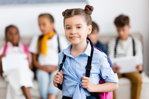 Selective focus of girl with backpack looking at camera in school  - Photo, Image