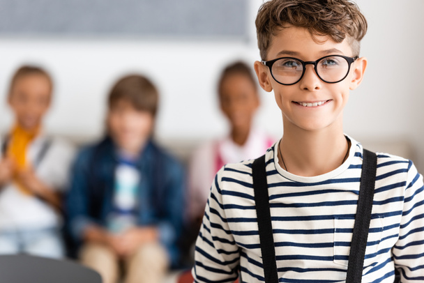 Selective focus of schoolboy in eyeglasses looking at camera in school  - Фото, зображення