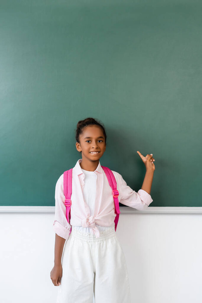 African american schoolgirl pointing with finger at chalkboard in classroom  - Фото, зображення