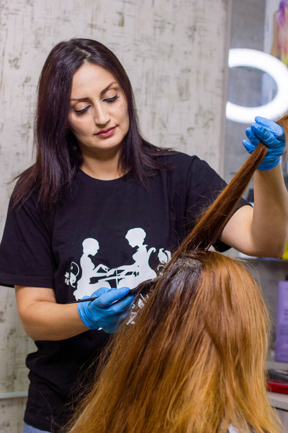 κομμώτρια στη δουλειά, νέα κομμώτρια βάφει τα μαλλιά του πελάτη - Φωτογραφία, εικόνα