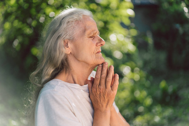 Harmaahiuksinen isoäiti rukoilee ulkona. Usko, hengellisyys ja uskonto käsite.  - Valokuva, kuva