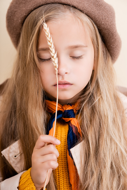 fashionable blonde girl with closed eyes in autumn outfit holding wheat spike - Fotó, kép