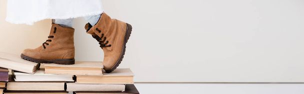 vista cortada de menina em botas marrons andando em livros vintage, tiro panorâmico - Foto, Imagem