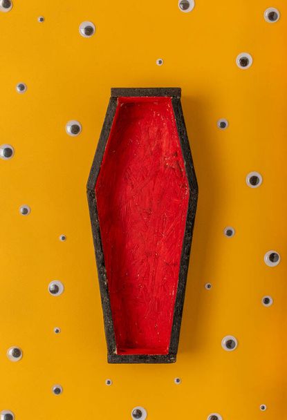 Halloween yellow background with an open red-black coffin in the center, around a scattering of plastic eyes of different sizes. A place for your product - Foto, imagen
