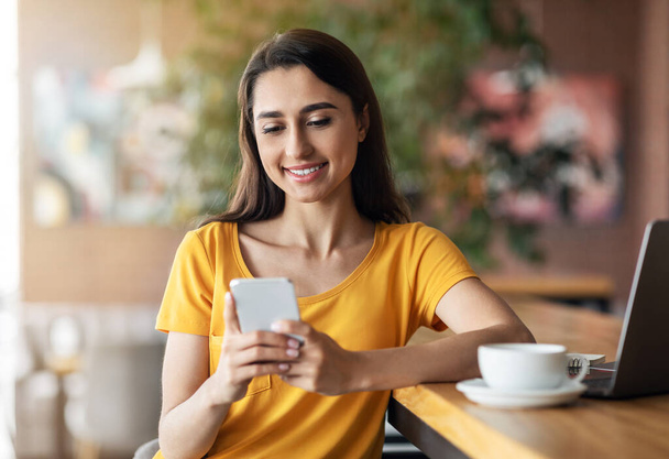 Boldog lány ül a kávézóban, teát iszik és okostelefon használata - Fotó, kép