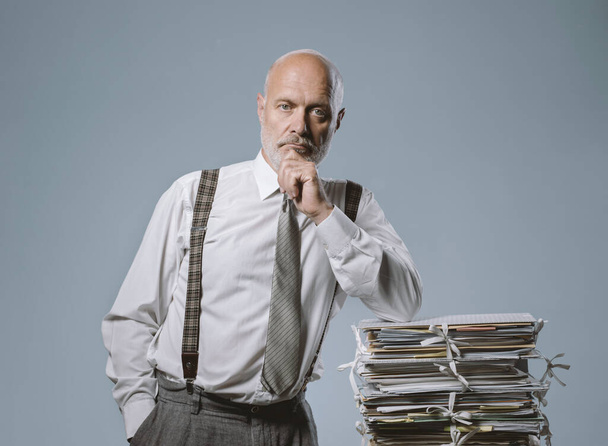 Confident businessman posing with a pile of paperwork, leadership and business concept - Φωτογραφία, εικόνα