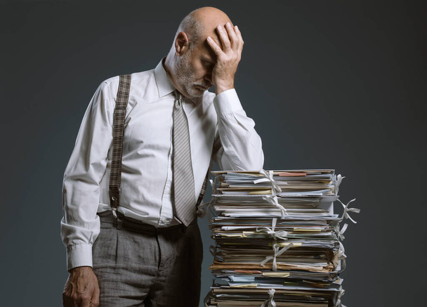 Pensive worried businessman leaning on a pile of paperwork, bureaucracy and administration concept - Фото, зображення