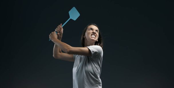 Angry woman killing mosquitoes, she is holding a fly swatter like a weapon - 写真・画像