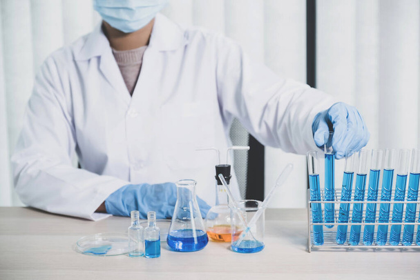A tudósok egy kék vegyi folyadékkal töltött üvegcsövet tartanak a kezükben kutatáshoz és elemzéshez egy laboratóriumban.. - Fotó, kép