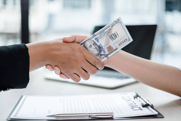photo of Businessmen shakes hands and dollar note, sign a contract to bribe corruption in the company. The concept of bribery and corruption. - Photo, Image