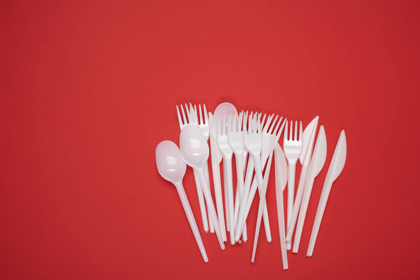 pile de fourchettes et cuillères en plastique sur fond rouge, vue du dessus, espace de copie - Photo, image