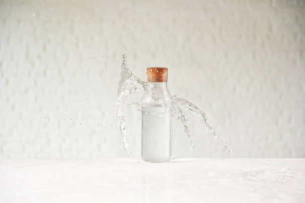 Water splash in the glass cup on the white table, brick wall background. - Foto, Imagen