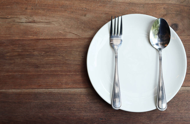 Белая тарелка, ложка и набор для практики на обеденном столе, вид сверху (справа от обеденного стола)). - Фото, изображение