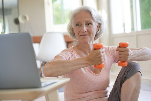 Senior woman doing fitness exercises with virtual class - Foto, Bild